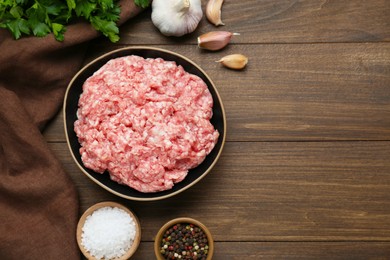 Photo of Bowl of raw fresh minced meat and ingredients on wooden table, flat lay. Space for text