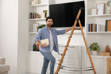 Photo of Man with books on wooden folding ladder at home