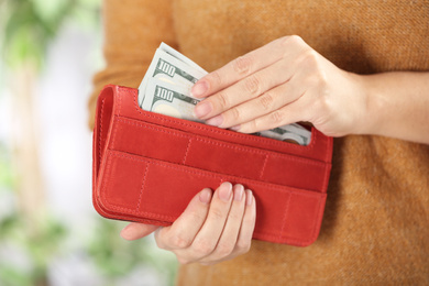 Photo of Woman putting money into wallet on blurred background, closeup