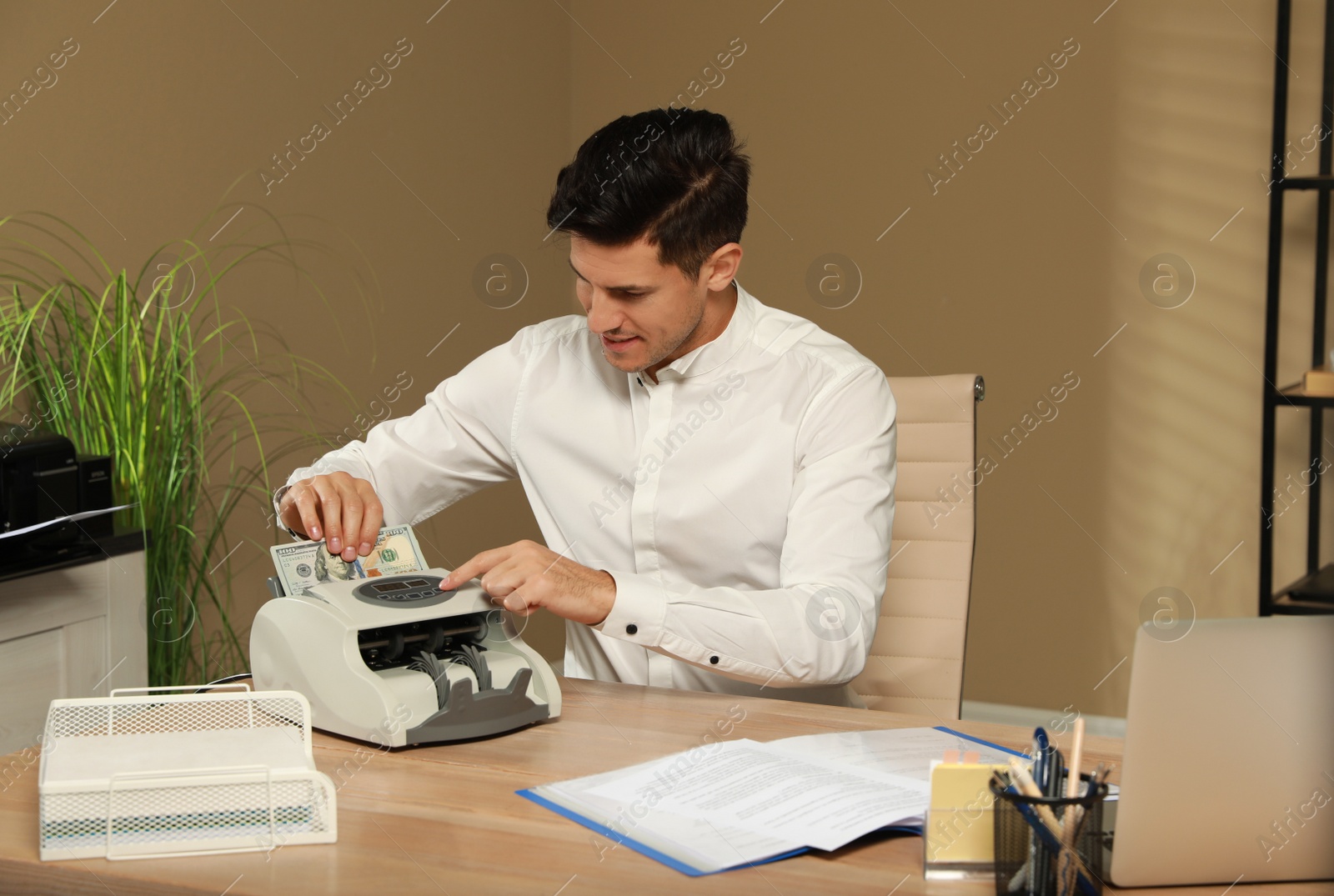Photo of Man putting money into banknote counter at wooden table indoors