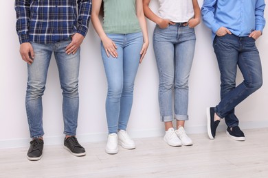 Photo of Group of people in stylish jeans near white wall indoors, closeup