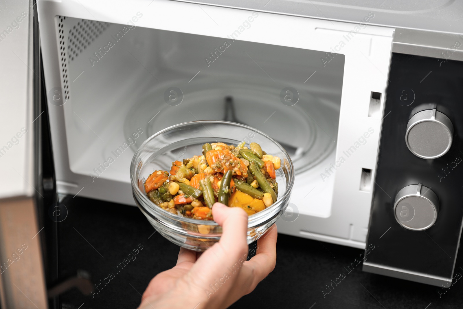 Photo of Young woman using microwave oven in kitchen, closeup
