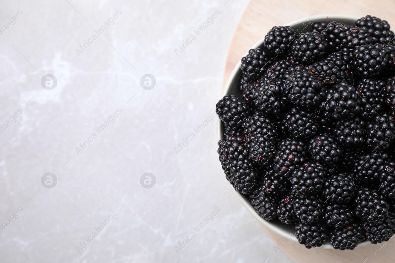 Photo of Fresh ripe blackberries in bowl on white table, top view. Space for text