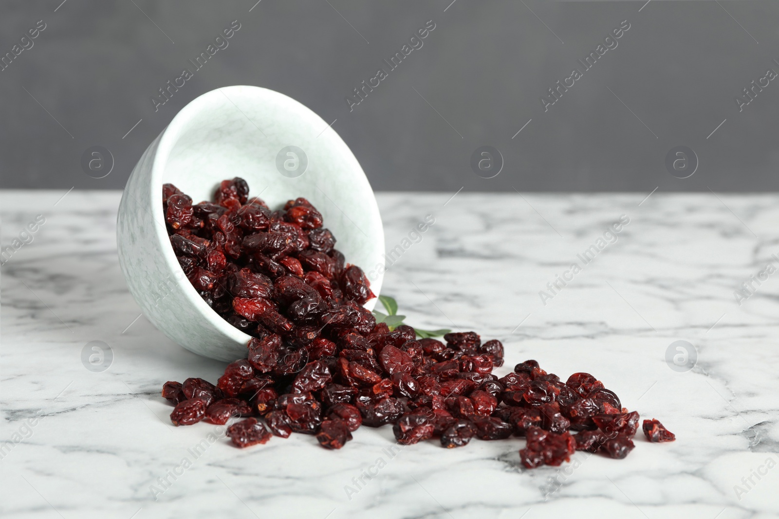 Photo of Overturned bowl with tasty dried cranberries on white marble table