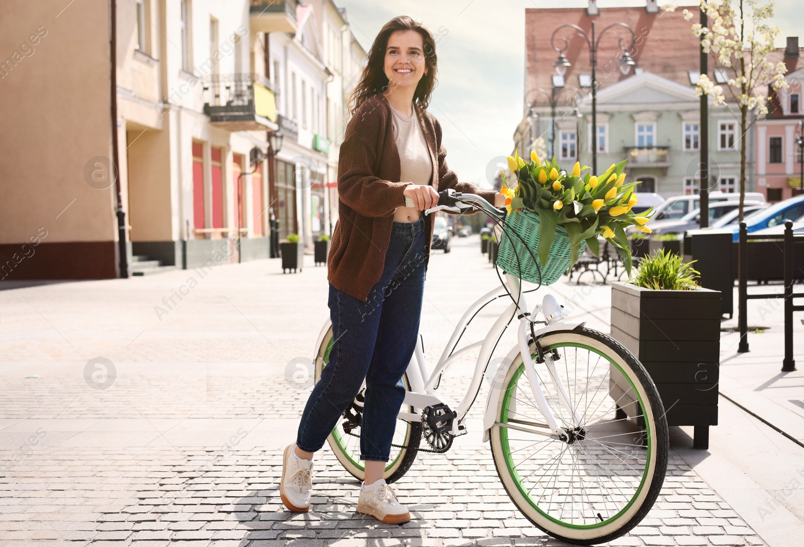 Photo of Beautiful woman with bicycle and bouquet of yellow tulips on city street