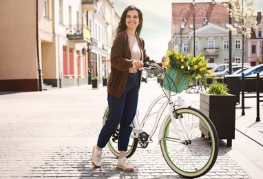 Photo of Beautiful woman with bicycle and bouquet of yellow tulips on city street