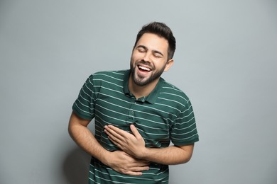 Young man laughing on light grey background. Funny joke