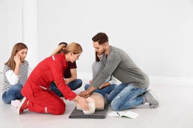 Photo of Group of people with instructor practicing CPR on mannequin at first aid class indoors