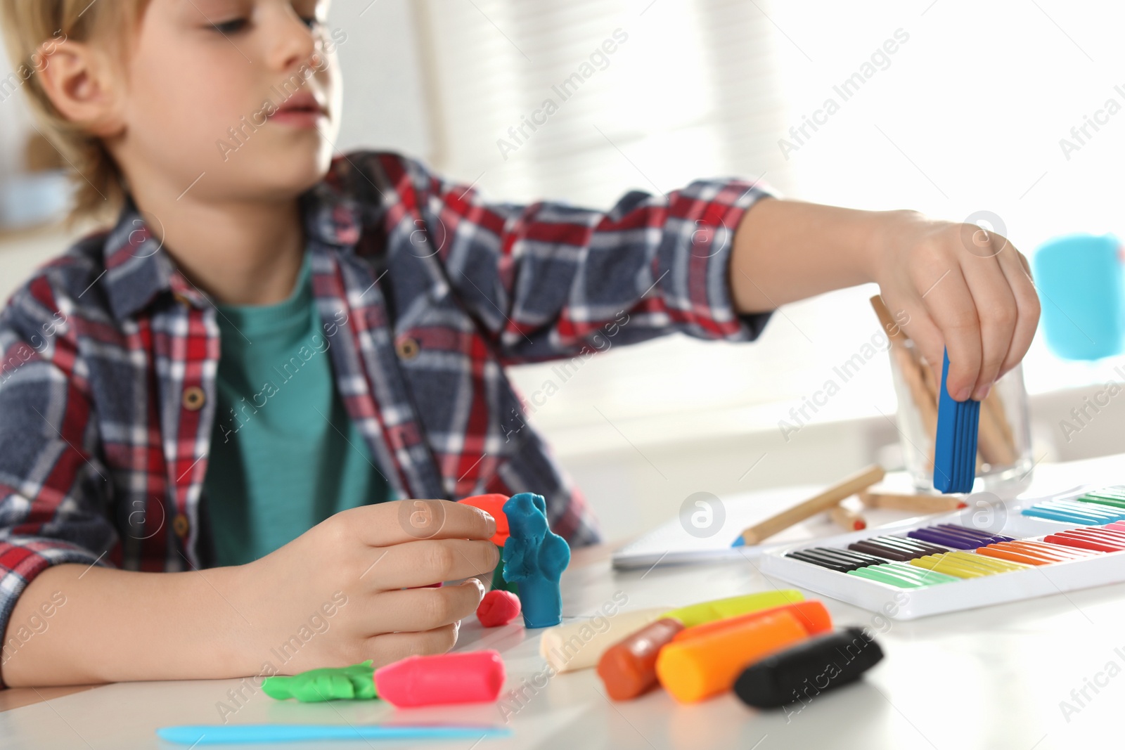 Photo of Little boy playing with plasticine at table indoors, closeup. Creative hobby