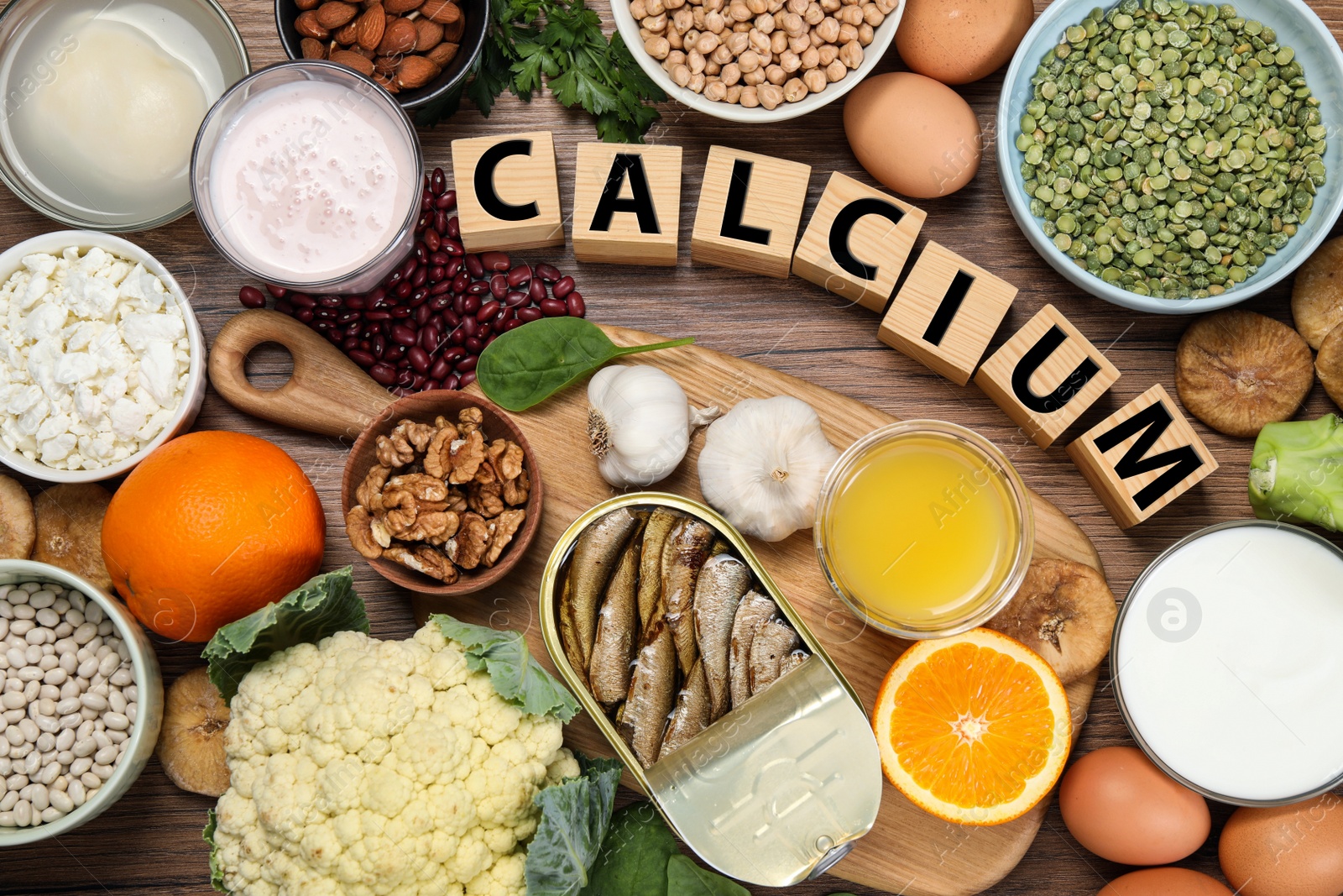 Photo of Set of natural food and cubes with word Calcium on wooden table, flat lay