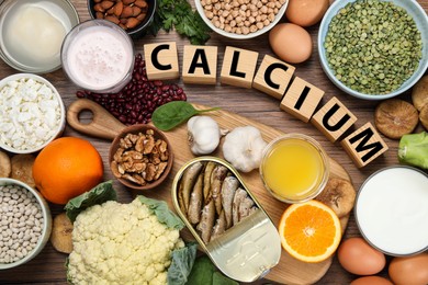 Photo of Setnatural food and cubes with word Calcium on wooden table, flat lay