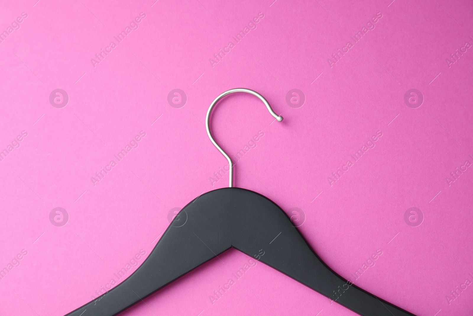 Photo of Empty black hanger on bright pink background, top view
