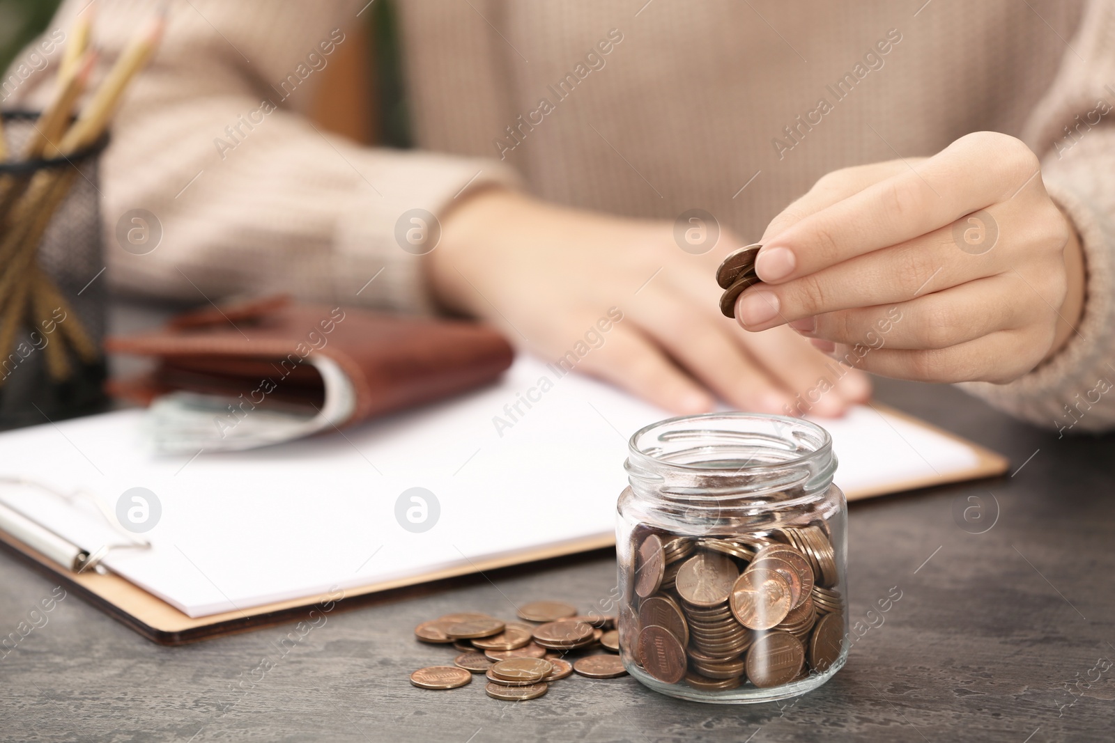 Photo of Woman putting money into glass jar at table, closeup