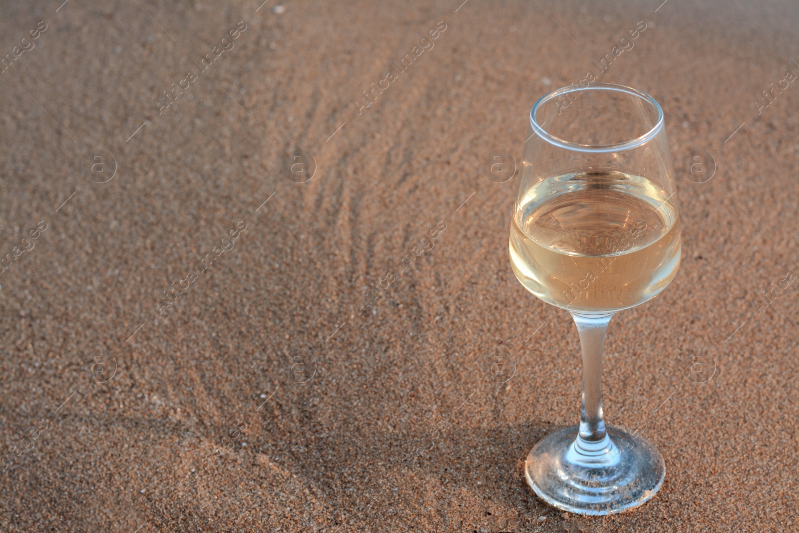 Photo of Glass of tasty wine on wet sand, space for text