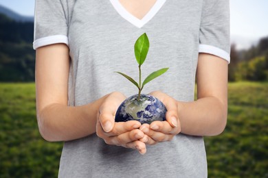 Make Earth green. Woman holding globe with seedling outdoors, closeup