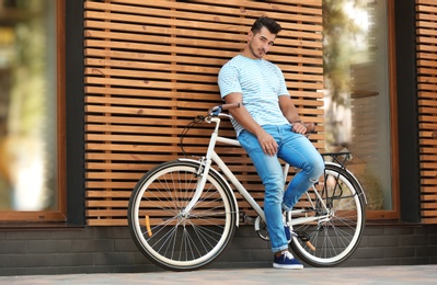 Photo of Handsome young hipster man with bicycle near wooden wall outdoors