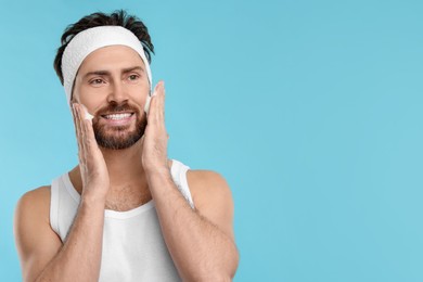 Photo of Man with headband washing his face on light blue background, space for text