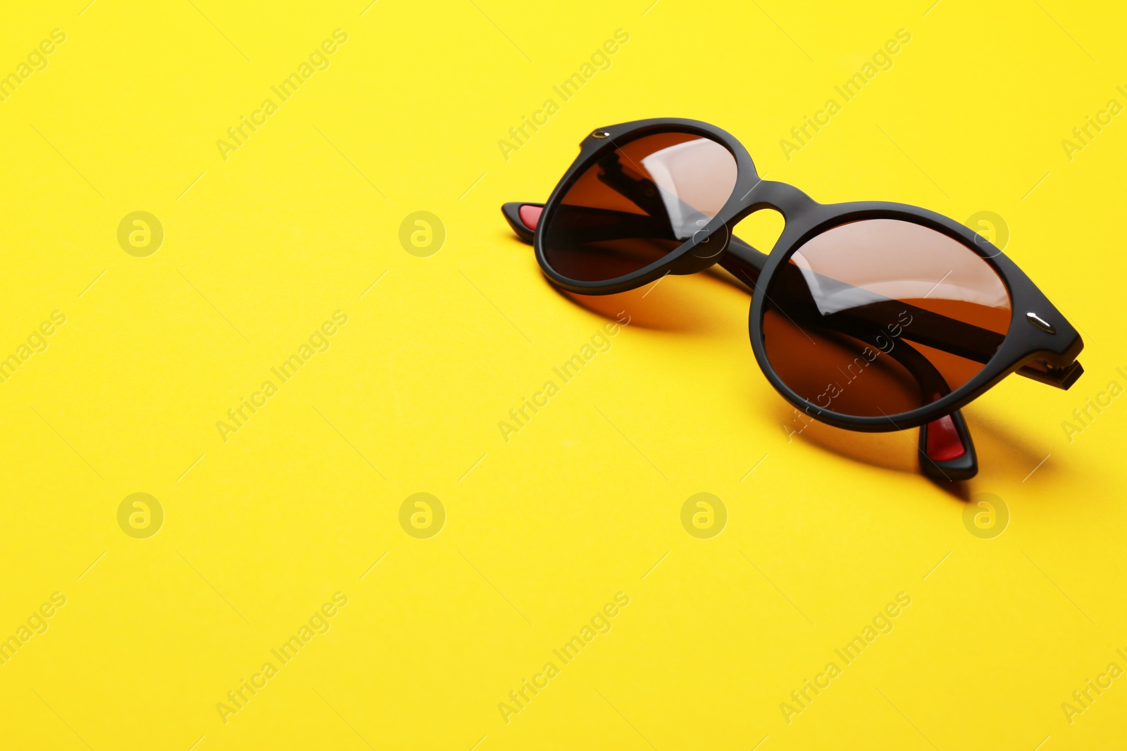 Photo of Stylish sunglasses on yellow background, space for text. Fashionable accessory