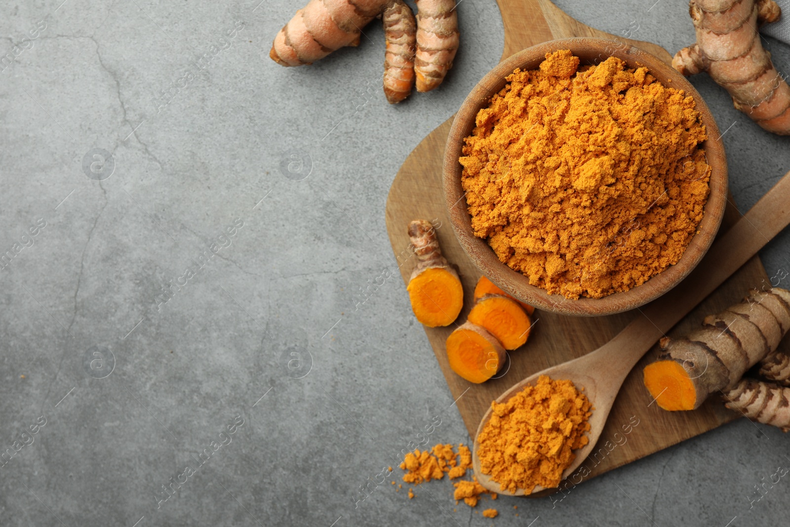 Photo of Aromatic turmeric powder and raw roots on grey table, flat lay. Space for text