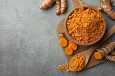 Photo of Aromatic turmeric powder and raw roots on grey table, flat lay. Space for text