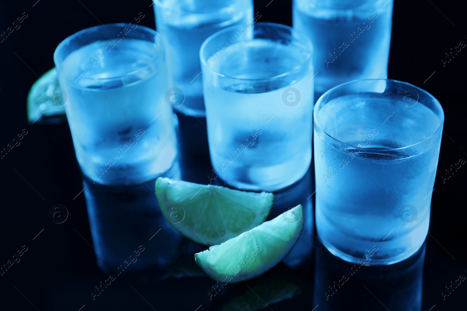 Photo of Shot glasses of vodka with lime slices on dark background