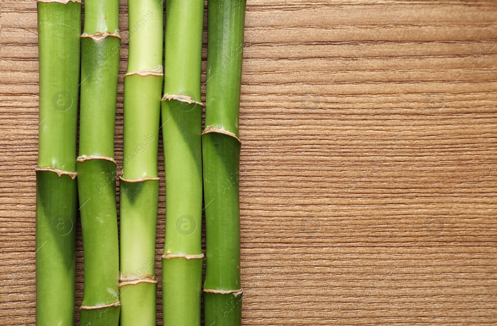 Photo of Green bamboo stems and space for text on wooden background, top view