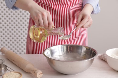 Photo of Woman pouring oil into spoon at white wooden table indoors, closeup. Cooking traditional grissini
