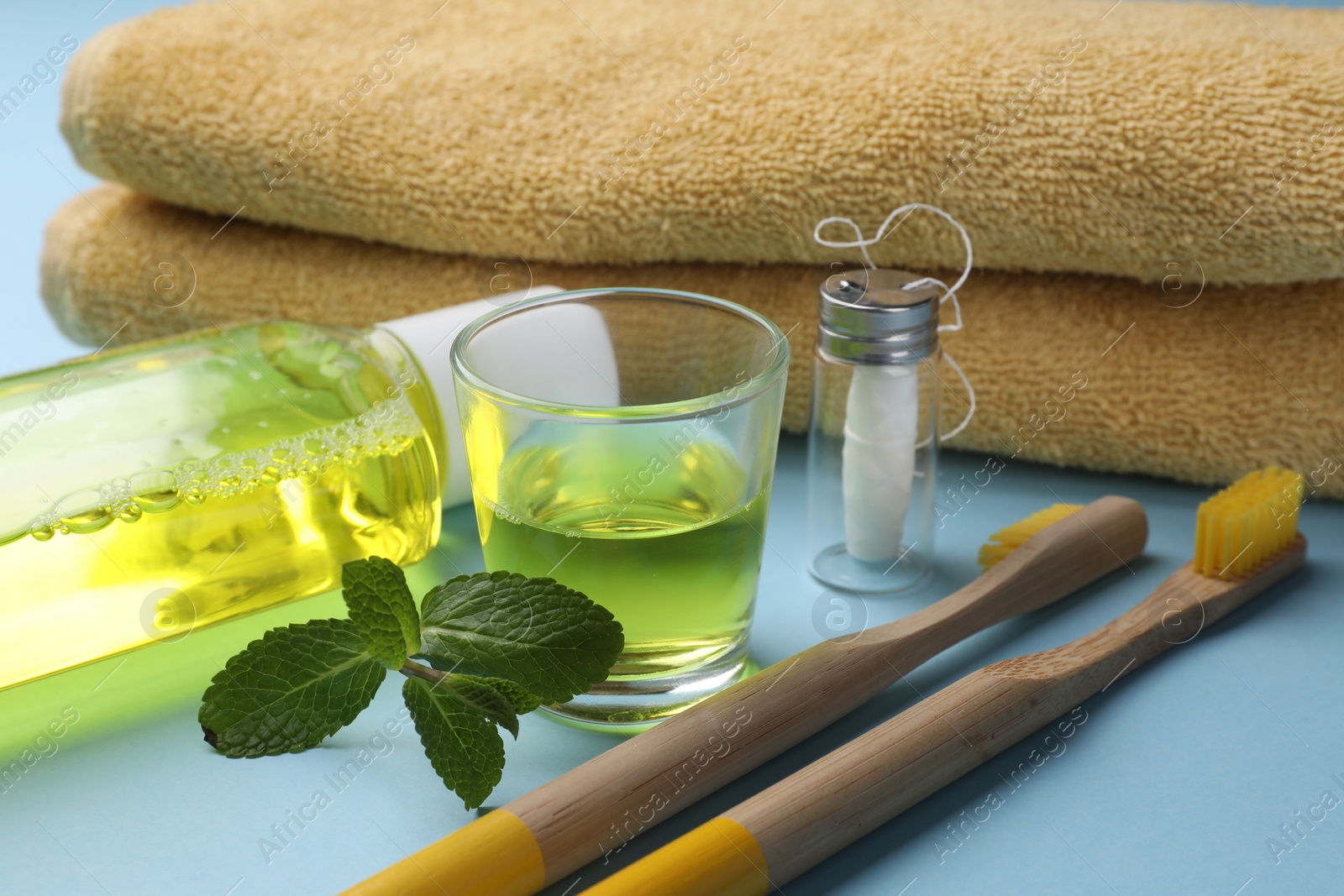 Photo of Fresh mouthwash, towel, toothbrushes and dental floss on light blue background, closeup