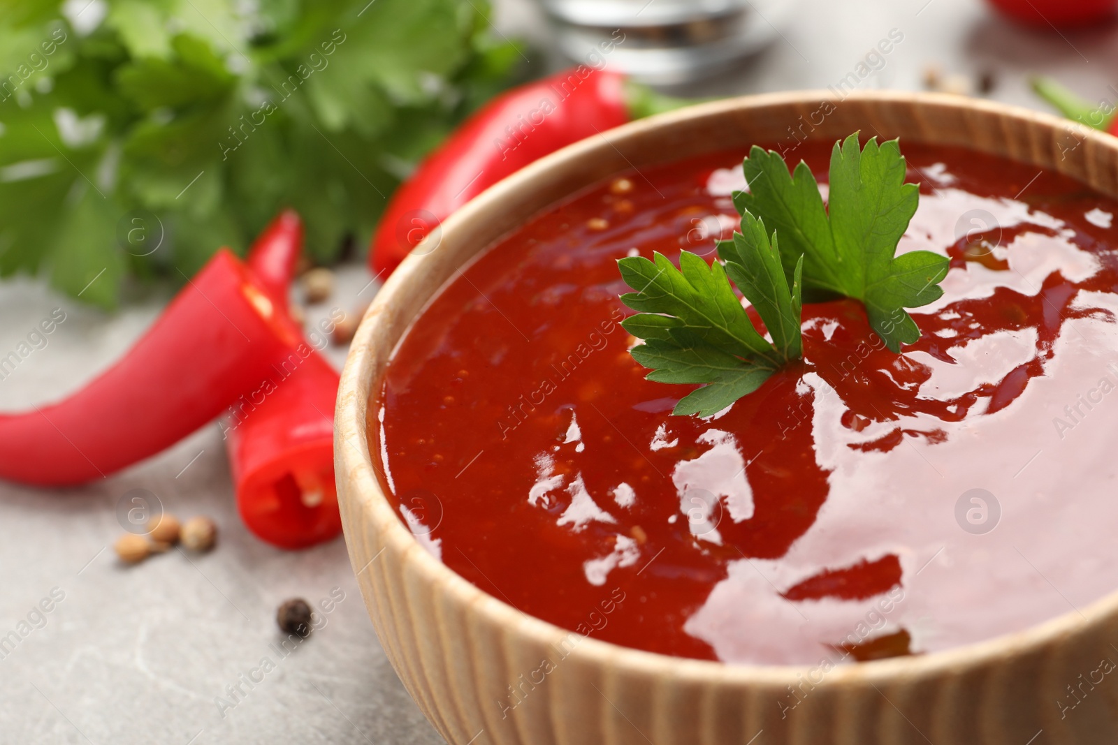 Photo of Spicy chili sauce with parsley in wooden bowl on light grey table, closeup