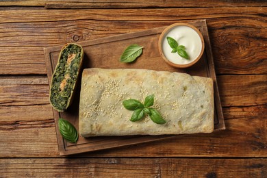 Cut tasty strudel with salmon, spinach, basil and sauce on wooden table, top view