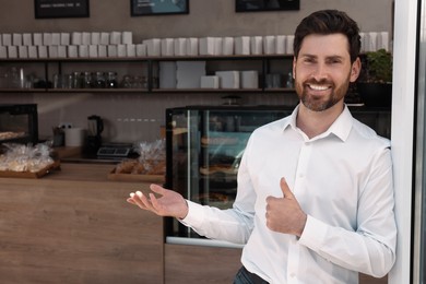 Photo of Happy business owner showing thumb up in bakery shop. Space for text