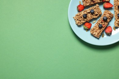 Photo of Tasty granola bars and berries on green background, top view. Space for text