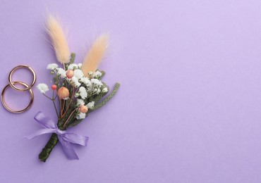 Photo of Small stylish boutonniere and rings on violet background, flat lay. Space for text
