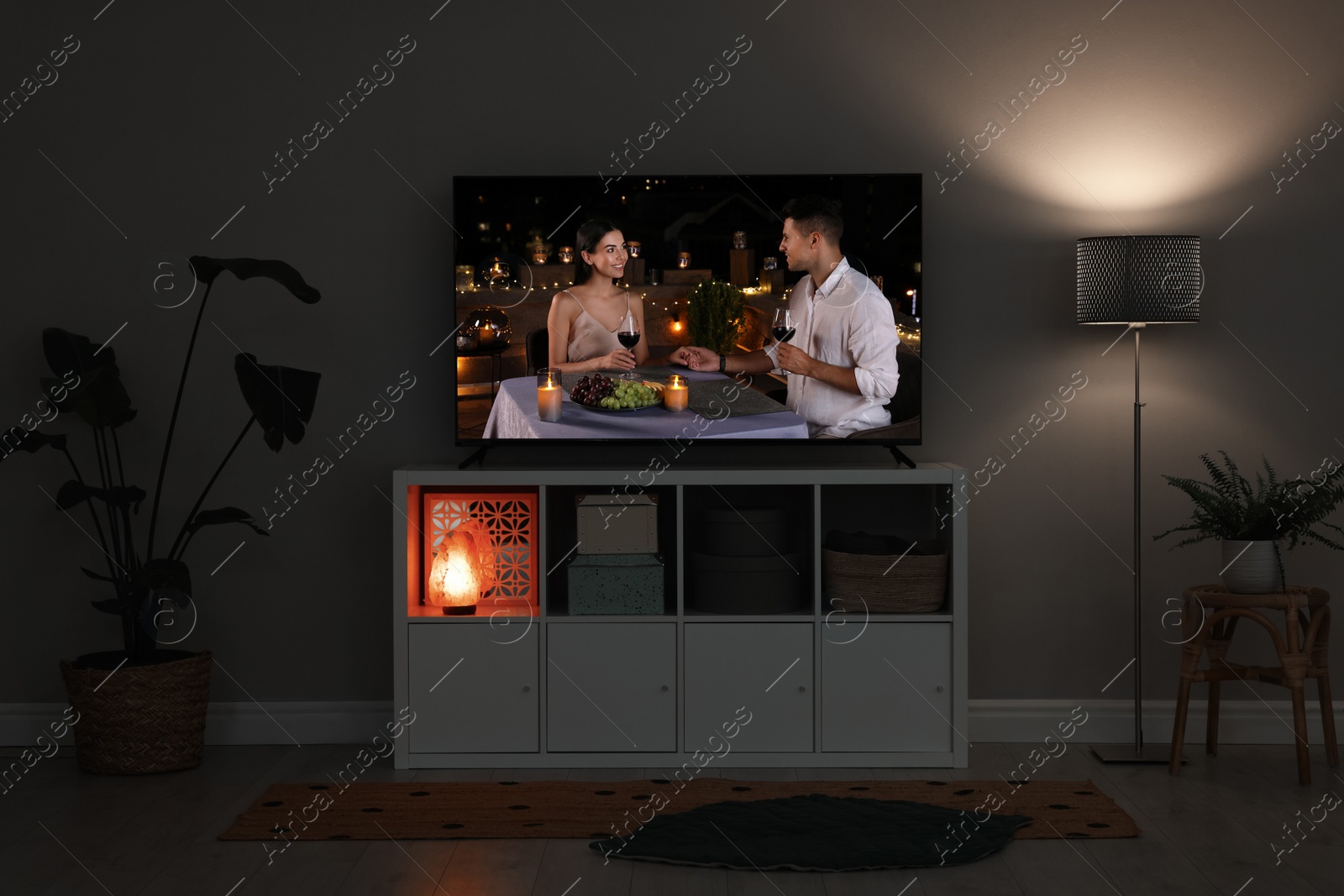 Image of Modern TV set on wooden stand in room. Scene of romantic movie on screen