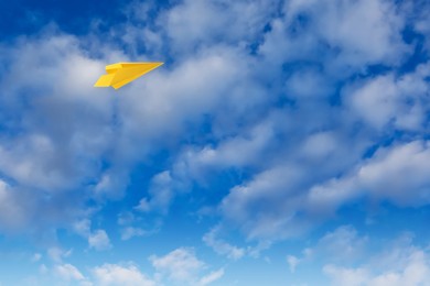 Image of Yellow paper plane flying in blue sky with clouds