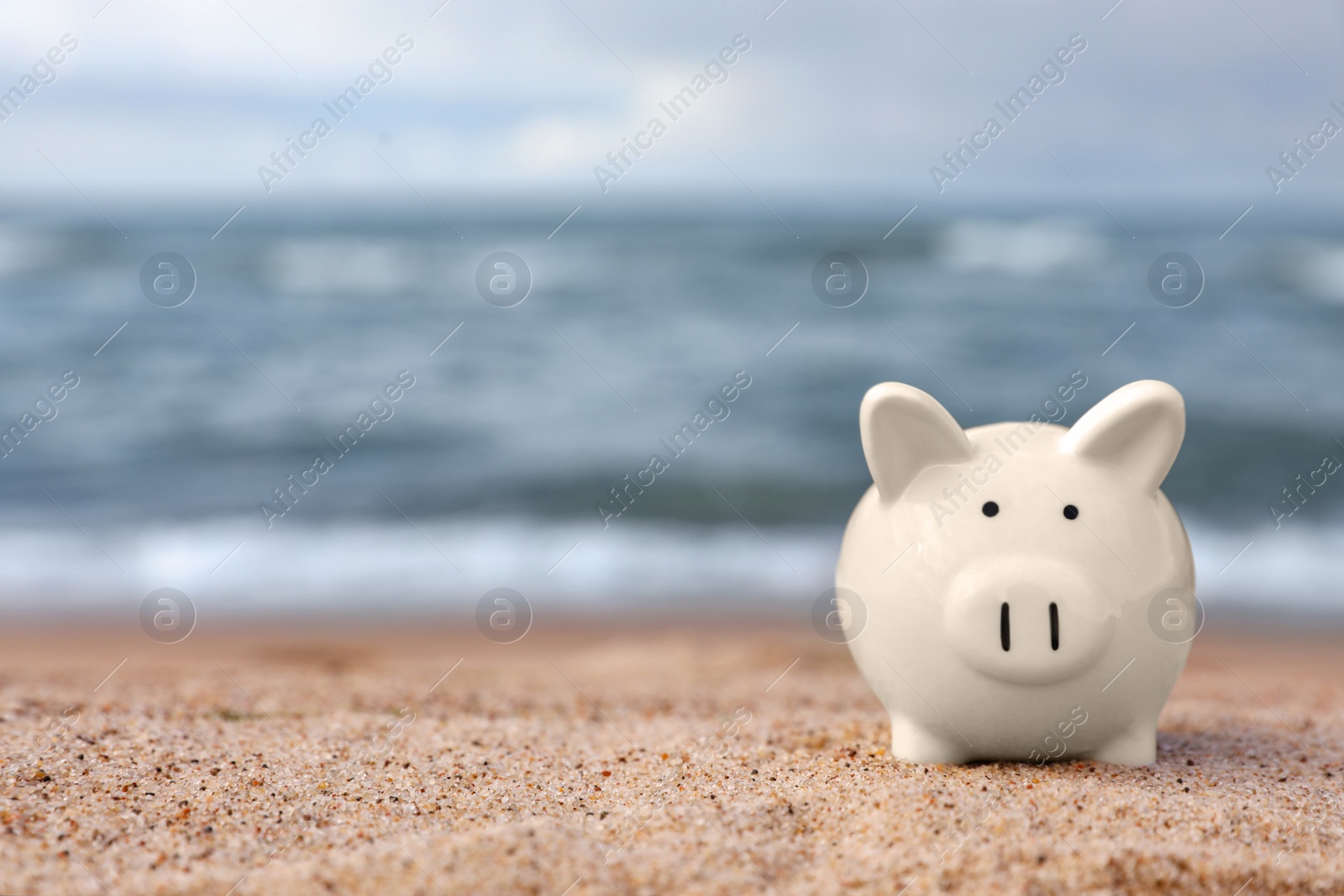 Photo of Cute piggy bank on sand near sea, space for text