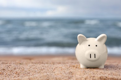 Cute piggy bank on sand near sea, space for text