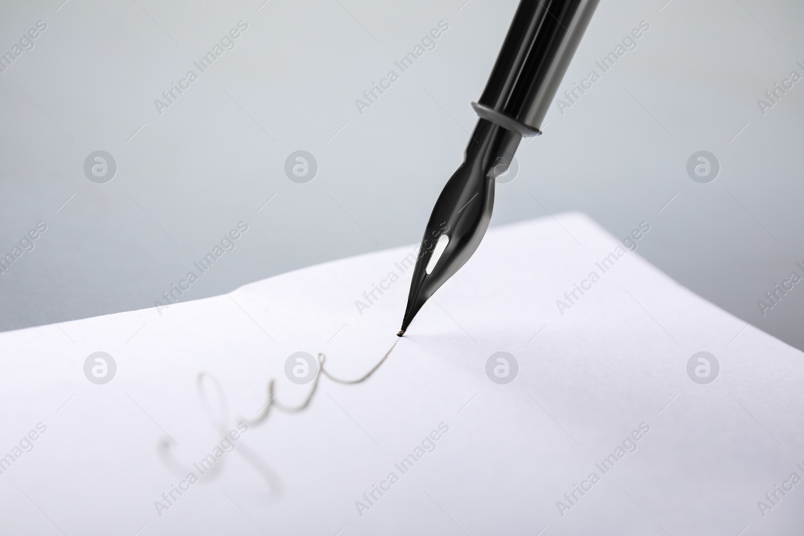 Photo of Signing on sheet of paper with fountain pen against light grey background, closeup