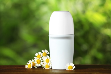 Photo of Natural female roll-on deodorant with chamomile flowers on wooden table against blurred green background