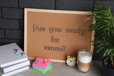 Cork board with phrase Are You Ready For Exams? on wooden table near black brick wall
