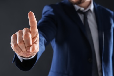 Photo of Businessman touching empty virtual screen against dark background, focus on hand