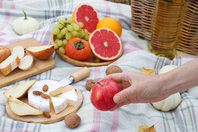 Photo of Woman taking apple from blanket with snacks and wine, closeup. Autumn picnic