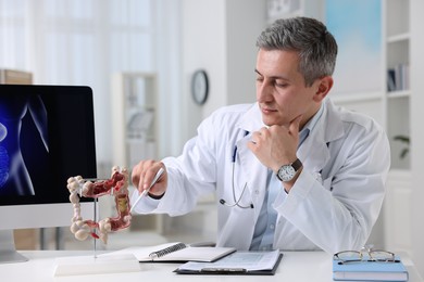Gastroenterologist showing anatomical model of large intestine at table in clinic
