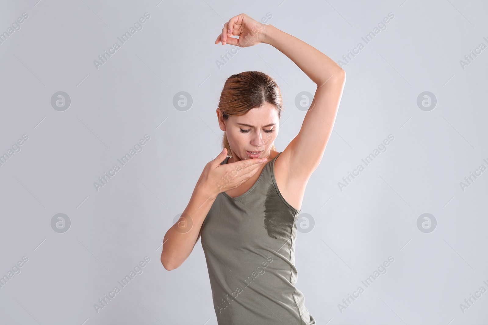 Photo of Young woman with sweat stain on her clothes against light background. Using deodorant