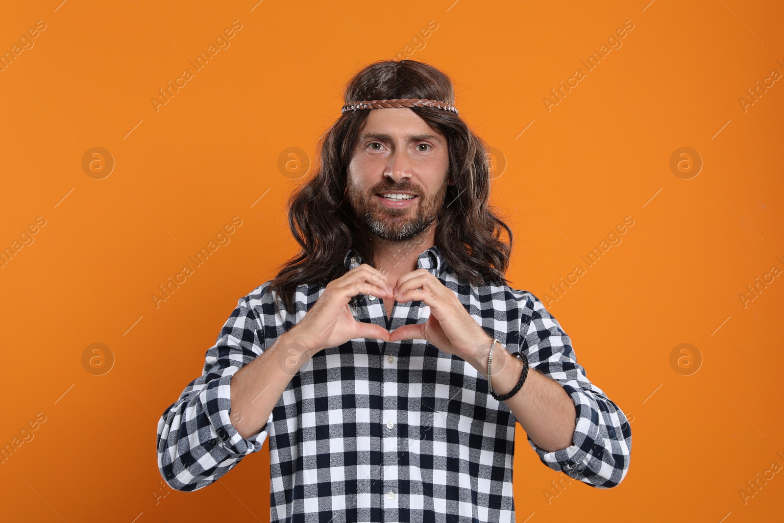 Photo of Hippie man making heart with hands on orange background