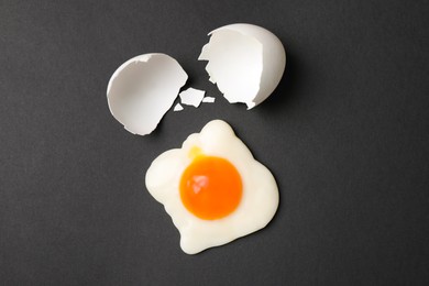 Photo of Sweet gummy fried egg and broken shell of real one on black background, flat lay. April Fools' Day