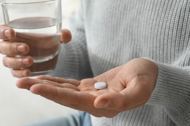 Photo of Man with glass of water and pill on blurred background, closeup