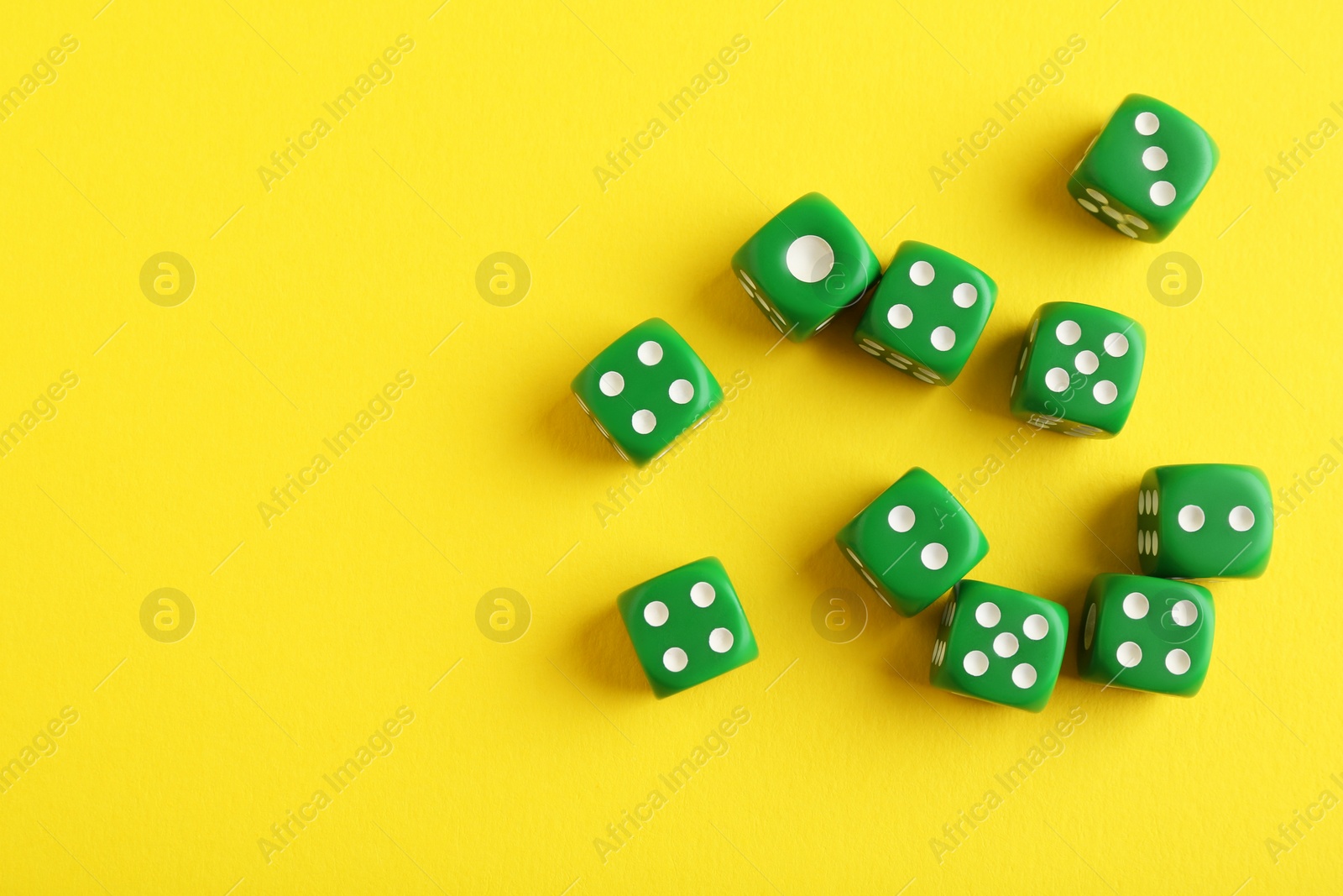 Photo of Many green game dices on yellow background, flat lay. Space for text