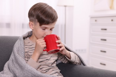 Photo of Cute boy drinking from red ceramic mug on sofa at home, space for text