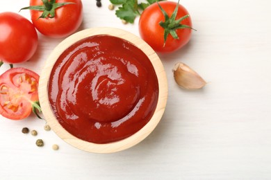 Photo of Delicious ketchup in bowl, peppercorns and tomatoes on white wooden table, flat lay. Space for text